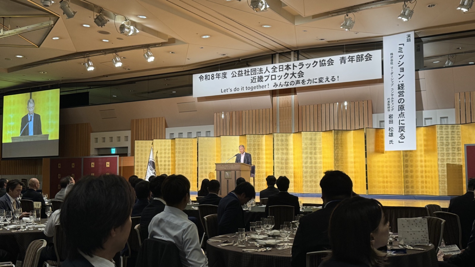 令和8年度 全日本トラック協会青年部会 近畿ブロック大会の式典・研修会ステージと大会スローガンの垂れ幕